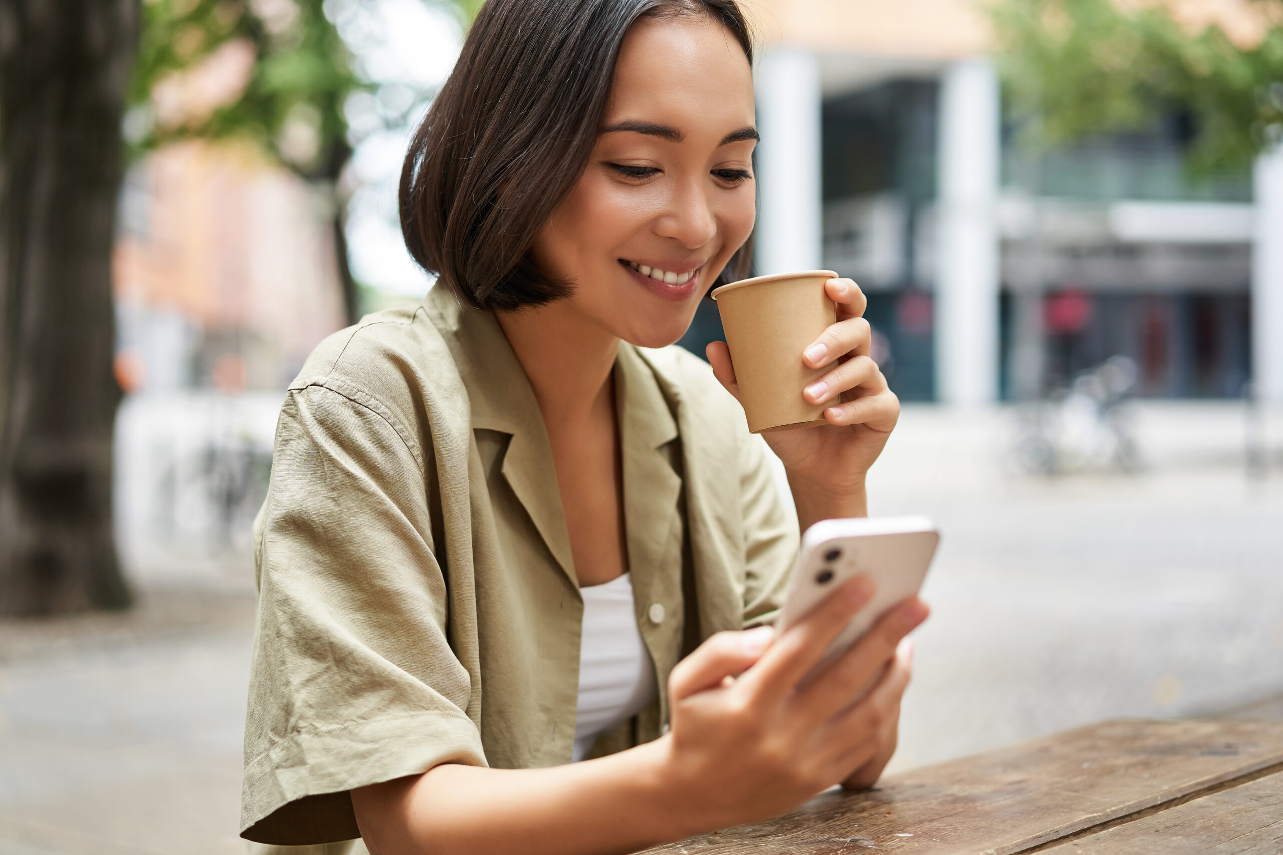 Young woman at an outdoor café drinking coffee and reading her smartphone
