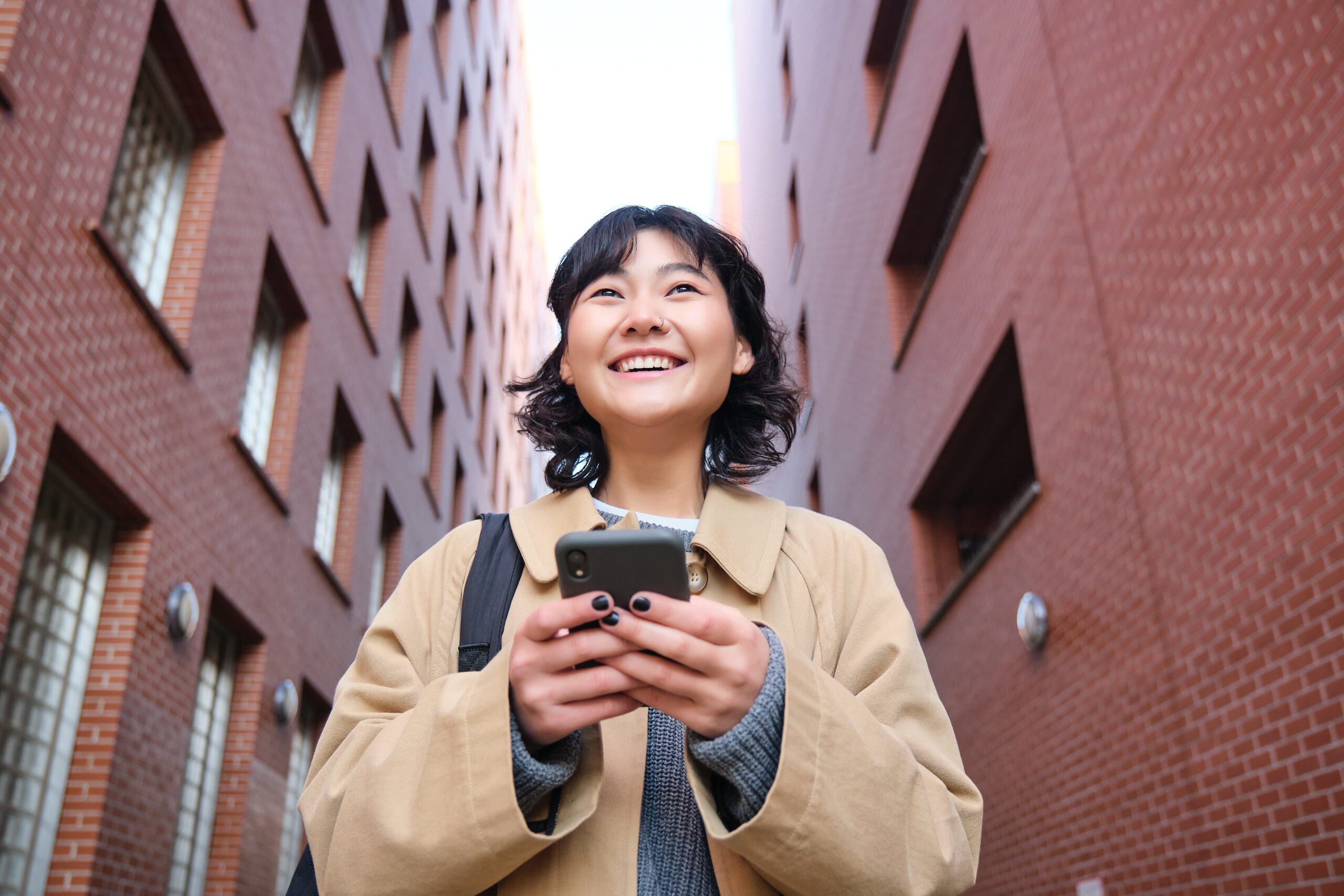 Young woman in headphones walking down a street while reading a message on her smartphone